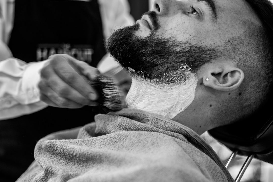 Barbiere che stende la schiuma da barba con il pennello